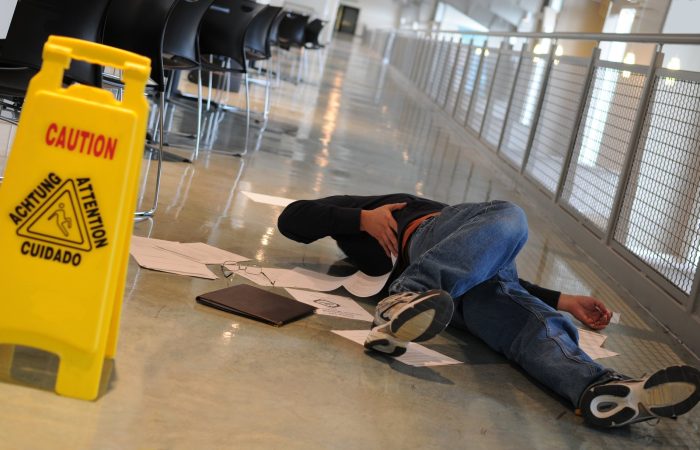 A man who slipped on a wet floor beside a bright yellow caution sign holds his back in pain
